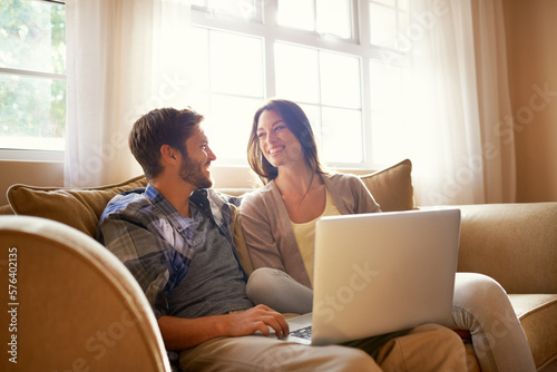 Smiling together over social media. Shot of a happy young couple using a laptop while sitting on the sofa. © Marius V/peopleimages.com