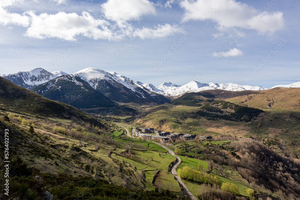paisaje de un valle verde con un pueblo y montañas nevadas en el segundo plano con cielo azul y algunas nubes