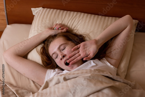 Tired girl yawns lying in bed