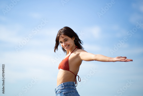 Fototapeta Naklejka Na Ścianę i Meble -  Pretty young woman standing with arms outstretched against sky