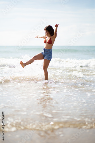 Excited young woman kicking water on the beach