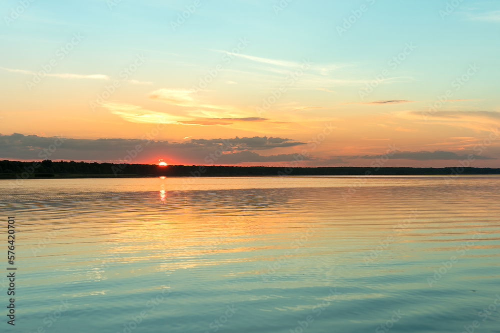 Sunset on the lake, the pink-gold sky is reflected in the water.