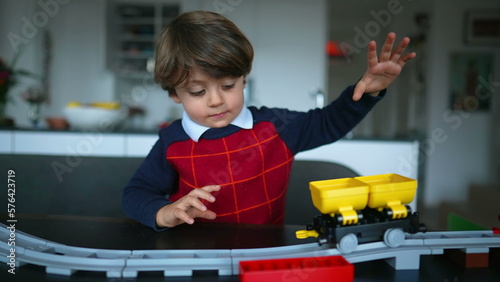 Small boy plays with train toy at home. One adorable 2 year old child plays alone with railroad gift at living room table