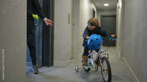 Mother and child leaving apartment. Little boy going out with bicycle standing at corridor by elevator door