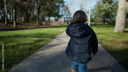 Back of child walking outside in park. One small boy wearing jacket strolling outdoors during sunny day in winter season