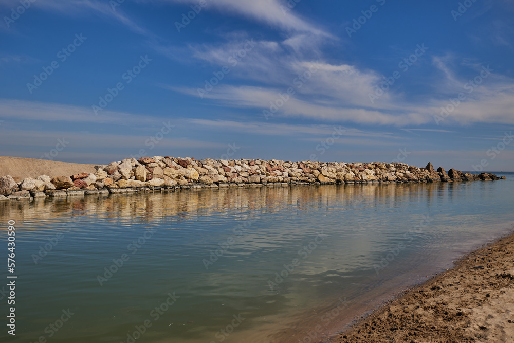 The river flows into the blue sea. The river is surrounded by stones and sand