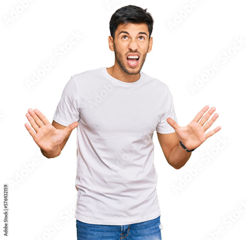 Young handsome man wearing casual white tshirt crazy and mad shouting and yelling with aggressive expression and arms raised. frustration concept.