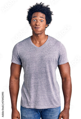 Handsome african american man with afro hair wearing casual clothes puffing cheeks with funny face. mouth inflated with air, crazy expression.