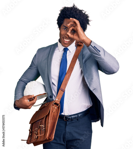 Handsome african american man with afro hair holding architect hardhat smiling happy doing ok sign with hand on eye looking through fingers