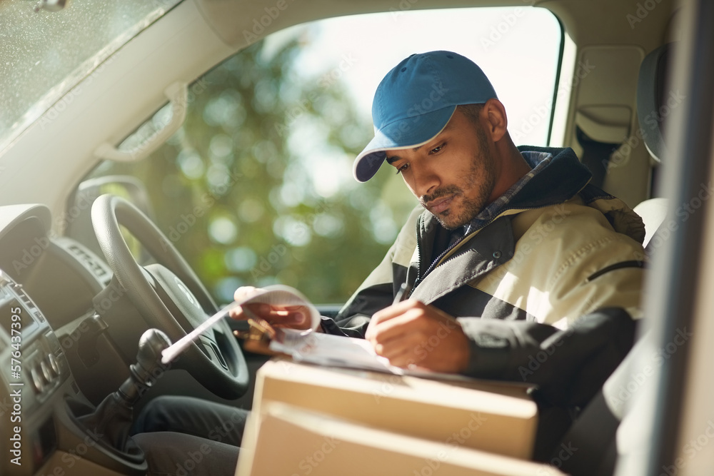 Updating his delivery status. Shot of a delivery man reading addresses while sitting in a delivery van. Updating his delivery status. Shot of a delivery man reading addresses while sitting in a delivery van.