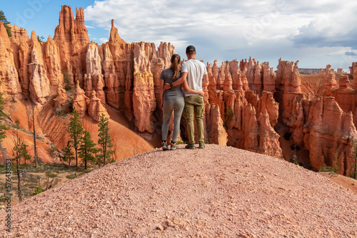 Hugging couple with scenic aerial view of hoodoo sandstone rock formations on Queens Garden trail, Bryce Canyon National Park, Utah, USA. Barren landscape surrounded by natural amphitheatre in summer