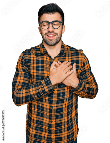 Hispanic man with beard wearing casual clothes and glasses smiling with hands on chest with closed eyes and grateful gesture on face. health concept.