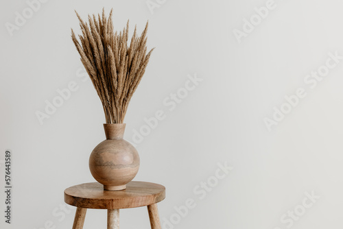 Brown wooden vase on a natural mango wooden stool with dried flowers in an empty room