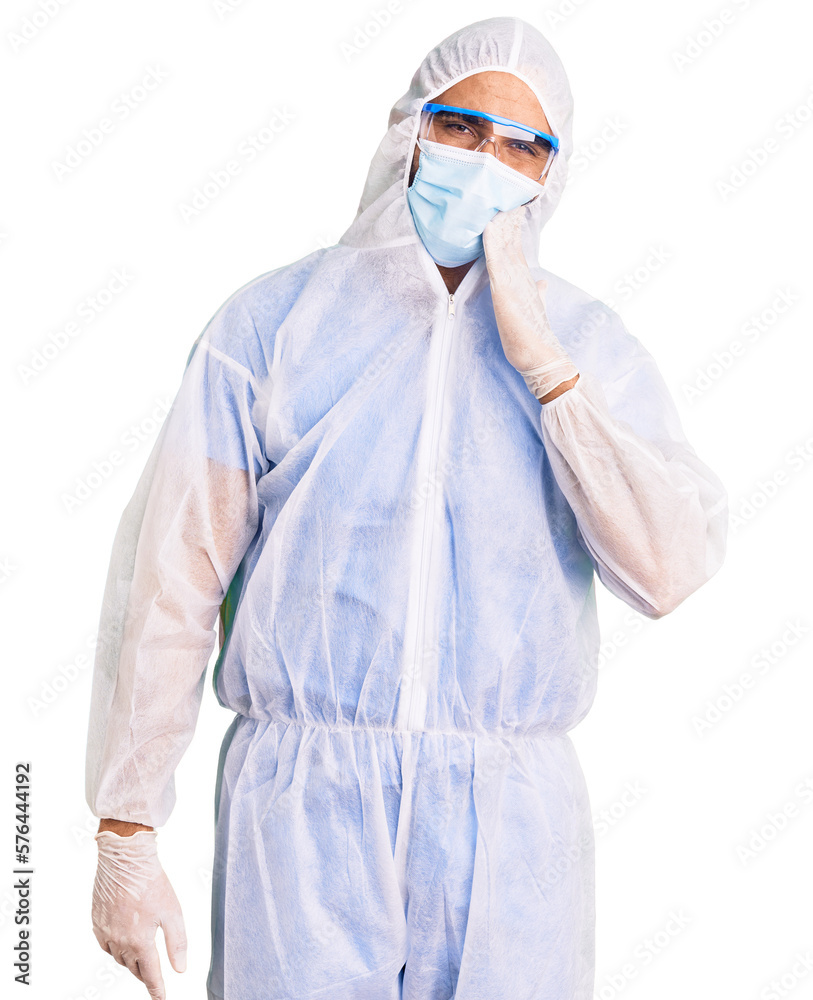Young hispanic man wearing doctor protection coronavirus uniform and medical mask touching mouth with hand with painful expression because of toothache or dental illness on teeth. dentist Young hispanic man wearing doctor protection coronavirus uniform and medical mask touching mouth with hand with painful expression because of toothache or dental illness on teeth. dentist