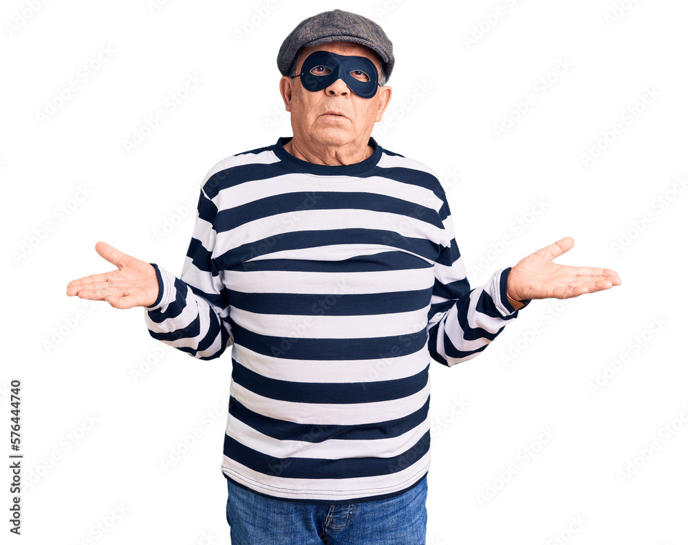 Senior handsome man wearing burglar mask and t-shirt clueless and confused with open arms, no idea concept. Senior handsome man wearing burglar mask and t-shirt clueless and confused with open arms, no idea concept.