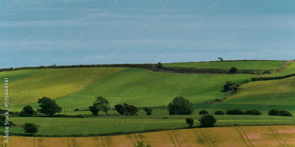 Picturesque agricultural landscape. Green hills under a blue sky. Hilly terrain in the south of Ireland, nature.