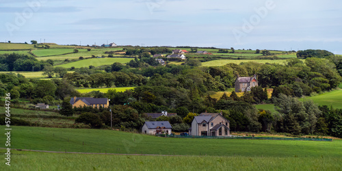 A small European village among green fields and trees. Farmhouses in Ireland. Picturesque agricultural landscape. Green fields under a blue sky, houses on green grass field.