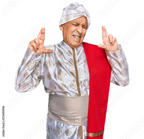 Photography Senior hispanic man wearing tradition sherwani saree clothes gesturing finger crossed smiling with hope and eyes closed
