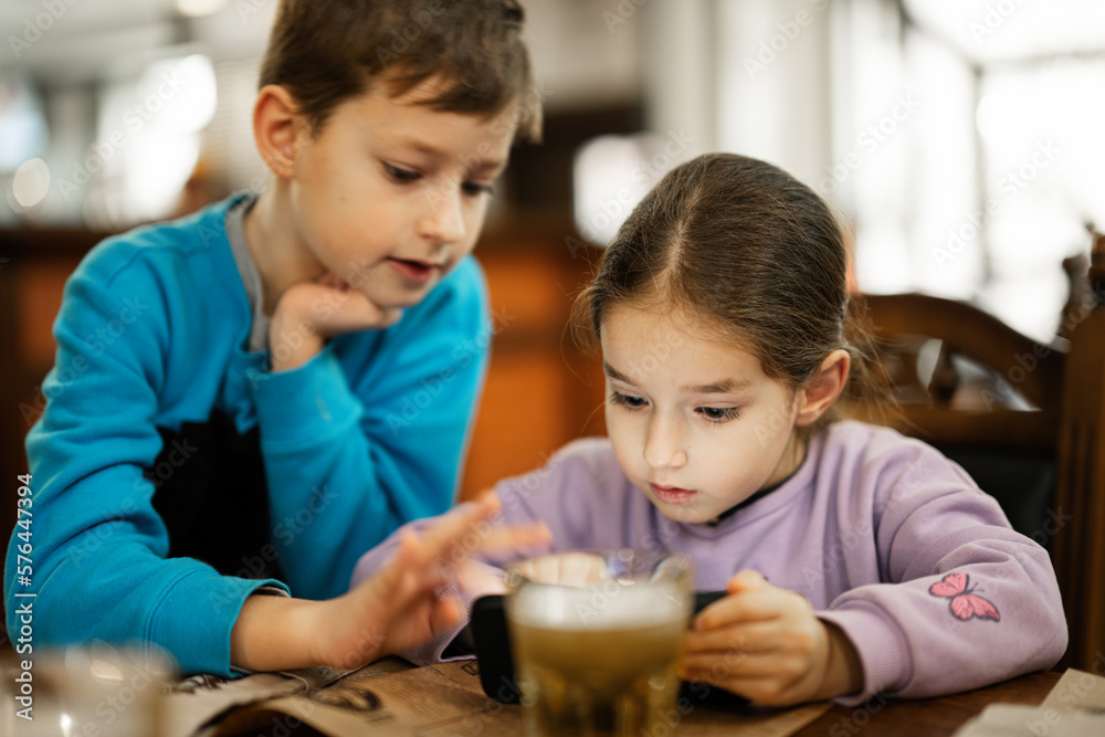 Brother with sister play in smartphone together, while eat in restaurant. Brother with sister play in smartphone together, while eat in restaurant.