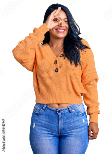 Hispanic woman with long hair wearing casual winter sweater doing ok gesture with hand smiling, eye looking through fingers with happy face.
