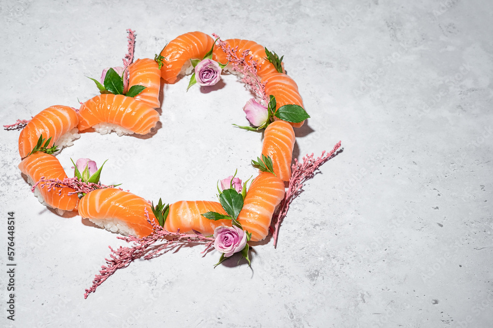 Sushi heart with flowers on grey background. Love sushi. Salmon nigiri with blooming roses. Women's day, Valentines day and spring celebration. Romantic dinner date. Creative Japanese set. Copy space
