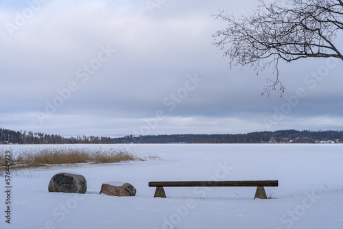 Wooden bench next to the frozen lake. Winter landscape from Finland.