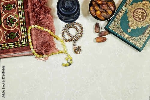 lantern and Holy Quran with Arabic calligraphy meaning of Al Quran and prayer mat , rosary muslim and dates fruits photo