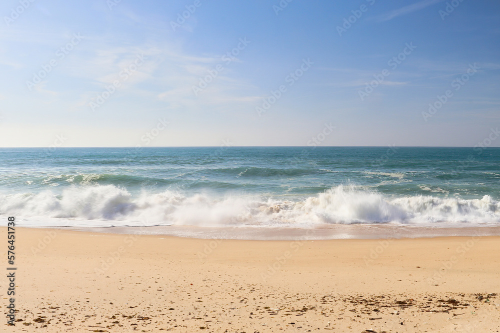 Sandy beach with waves in the ocean near Lisbon, Portugal on a sunny winter day.