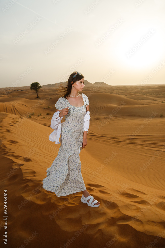 A young beautiful woman posing in a dress - against the background of a desert landscape. Abu Dhabi, UAE. A young beautiful woman posing in a dress - against the background of a desert landscape. Abu Dhabi, UAE.