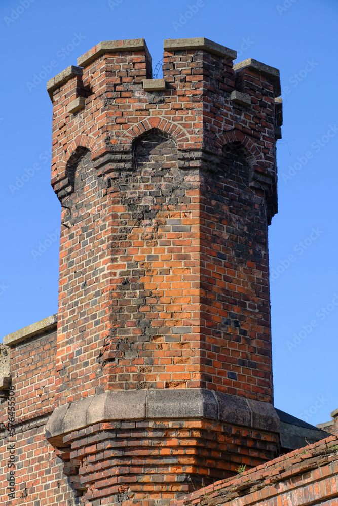 Crenellated fortress tower made red brick against blue sky background.
