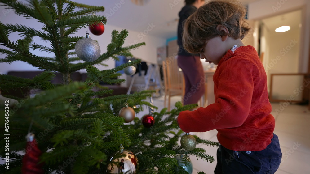 Child decorating Christmas tree. One small boy celebrating december festivities. Kid putting ball ornamentation