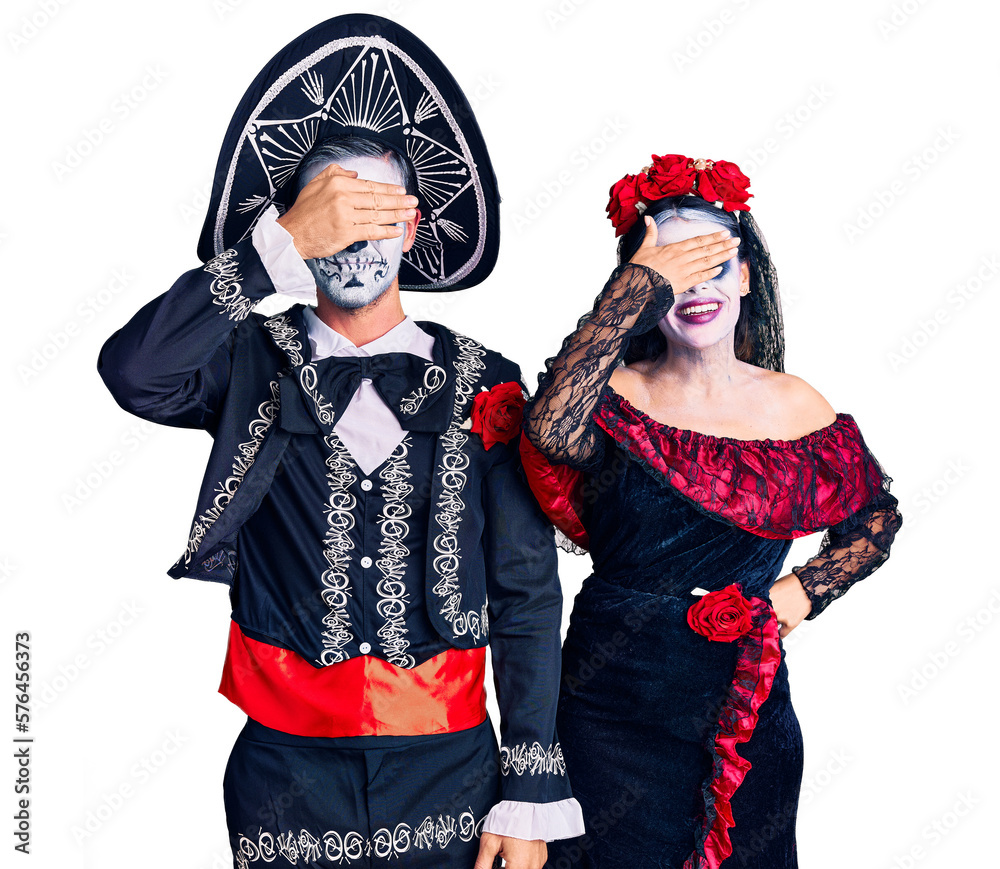 Young couple wearing mexican day of the dead costume over background smiling and laughing with hand on face covering eyes for surprise. blind concept.