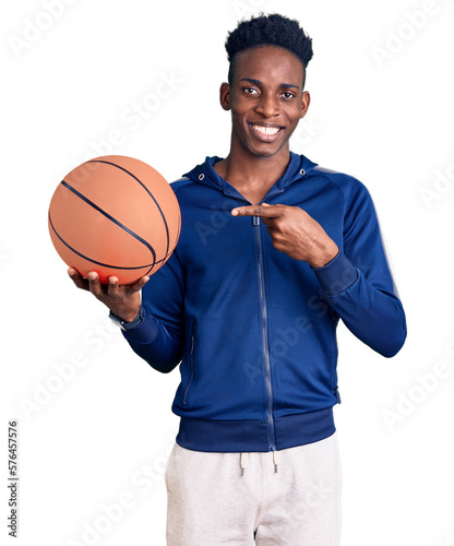Young african american man holding basketball ball smiling happy pointing with hand and finger