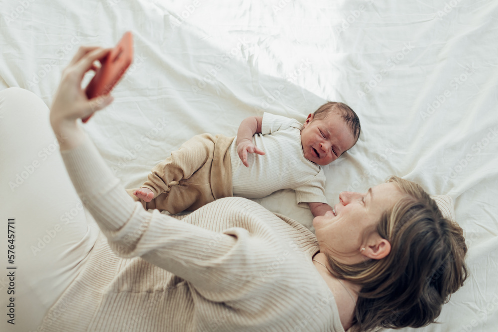 happy caucasian mother lying in bed with newborn son taking selfie or making video call happy caucasian mother lying in bed with newborn son taking selfie or making video call