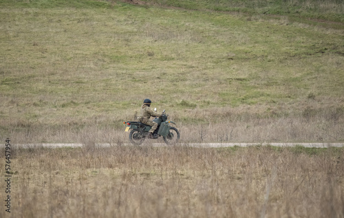 British army motorcycle dispatch rider in action across open countryside. Wiltshire UK