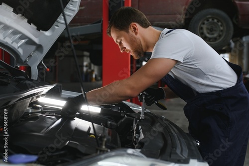Auto mechanic working on car engine in mechanics garage. Repair service.