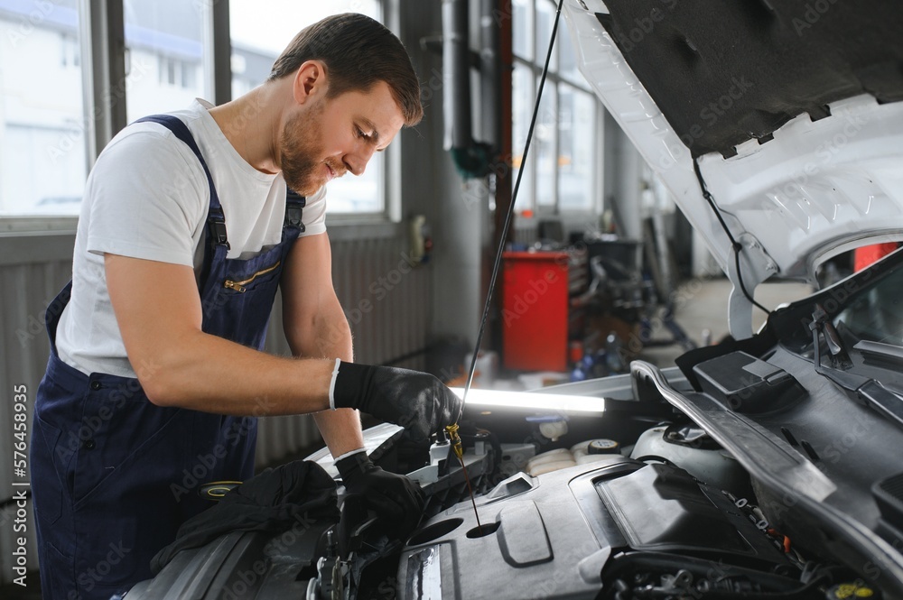 Auto mechanic checking the oil level in car engine,inspects engine water level dipstick,concept of checking the engine oil level every time before leaving. Auto mechanic checking the oil level in car engine,inspects engine water level dipstick,concept of checking the engine oil level every time before leaving.