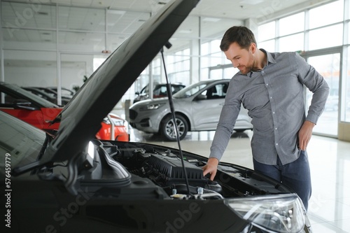 Looks under the hood of automobile. Young man in the car dealership.