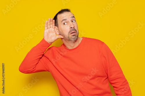 Listening Hispanic man holds his hand near his ear on a yellow background. Handsome man trying to listen to someone's conversation