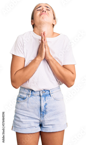 Young beautiful blonde woman wearing casual white tshirt begging and praying with hands together with hope expression on face very emotional and worried. begging. photo