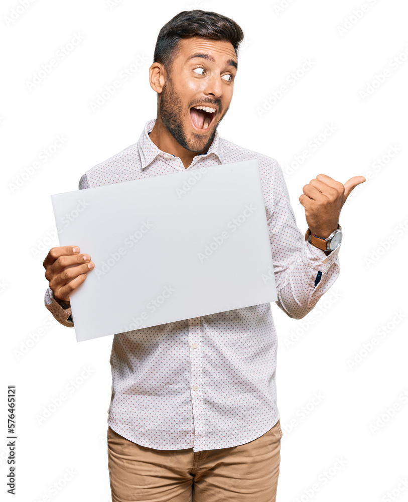 Handsome hispanic man holding blank empty banner pointing thumb up to the side smiling happy with open mouth Handsome hispanic man holding blank empty banner pointing thumb up to the side smiling happy with open mouth