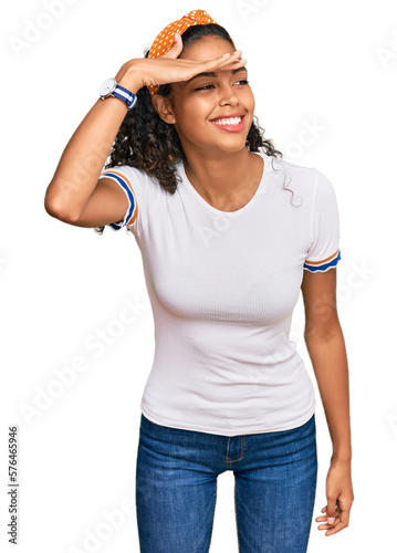 Young african american girl wearing casual clothes very happy and smiling looking far away with hand over head. searching concept.