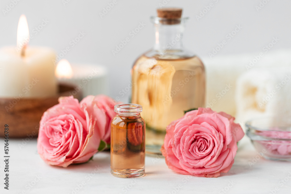 Aromatherapy. Concept of pure organic essential rose oil. Elixir with plant based floral or herbal ingredients. Pink flowers extract. Spa atmosphere with candle, towel. White background Aromatherapy. Concept of pure organic essential rose oil. Elixir with plant based floral or herbal ingredients. Pink flowers extract. Spa atmosphere with candle, towel. White background