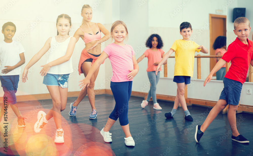 Fototapeta premium Group of tweens doing dance workout with female coach in classic choreography class..