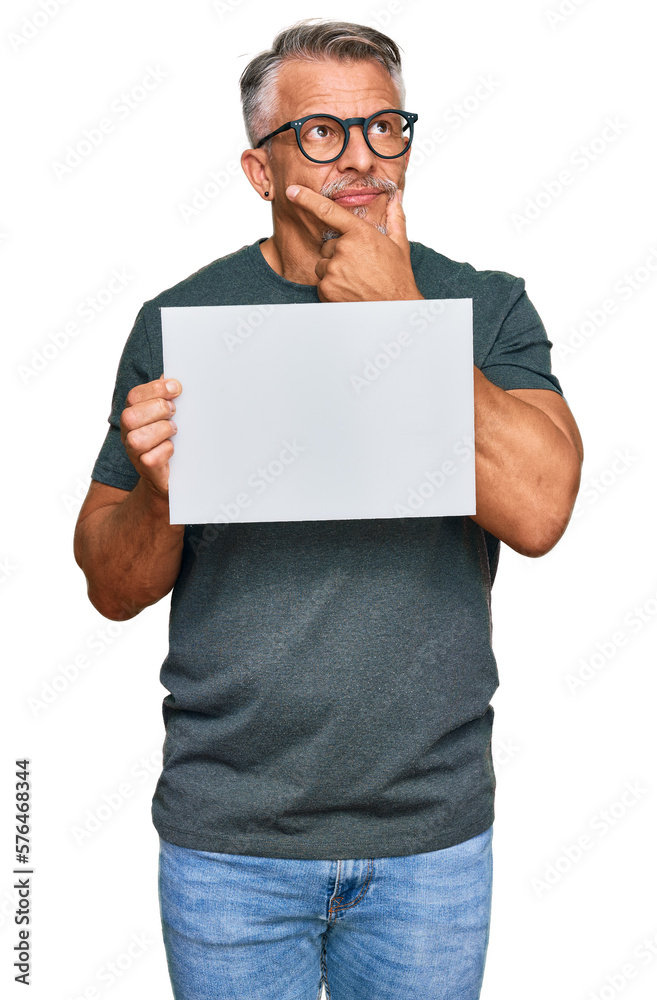 Middle age grey-haired man holding blank empty banner serious face thinking about question with hand on chin, thoughtful about confusing idea Middle age grey-haired man holding blank empty banner serious face thinking about question with hand on chin, thoughtful about confusing idea