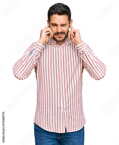 Young hispanic man wearing business shirt covering ears with fingers with annoyed expression for the noise of loud music. deaf concept.