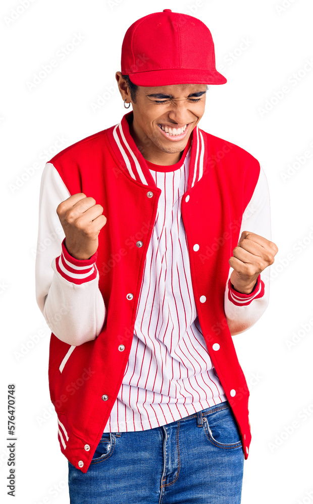 Young african amercian man wearing baseball uniform very happy and excited doing winner gesture with arms raised, smiling and screaming for success. celebration concept. Young african amercian man wearing baseball uniform very happy and excited doing winner gesture with arms raised, smiling and screaming for success. celebration concept.