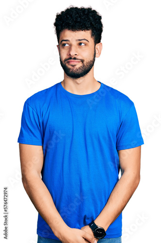 Young arab man with beard wearing casual blue t shirt smiling looking to the side and staring away thinking.