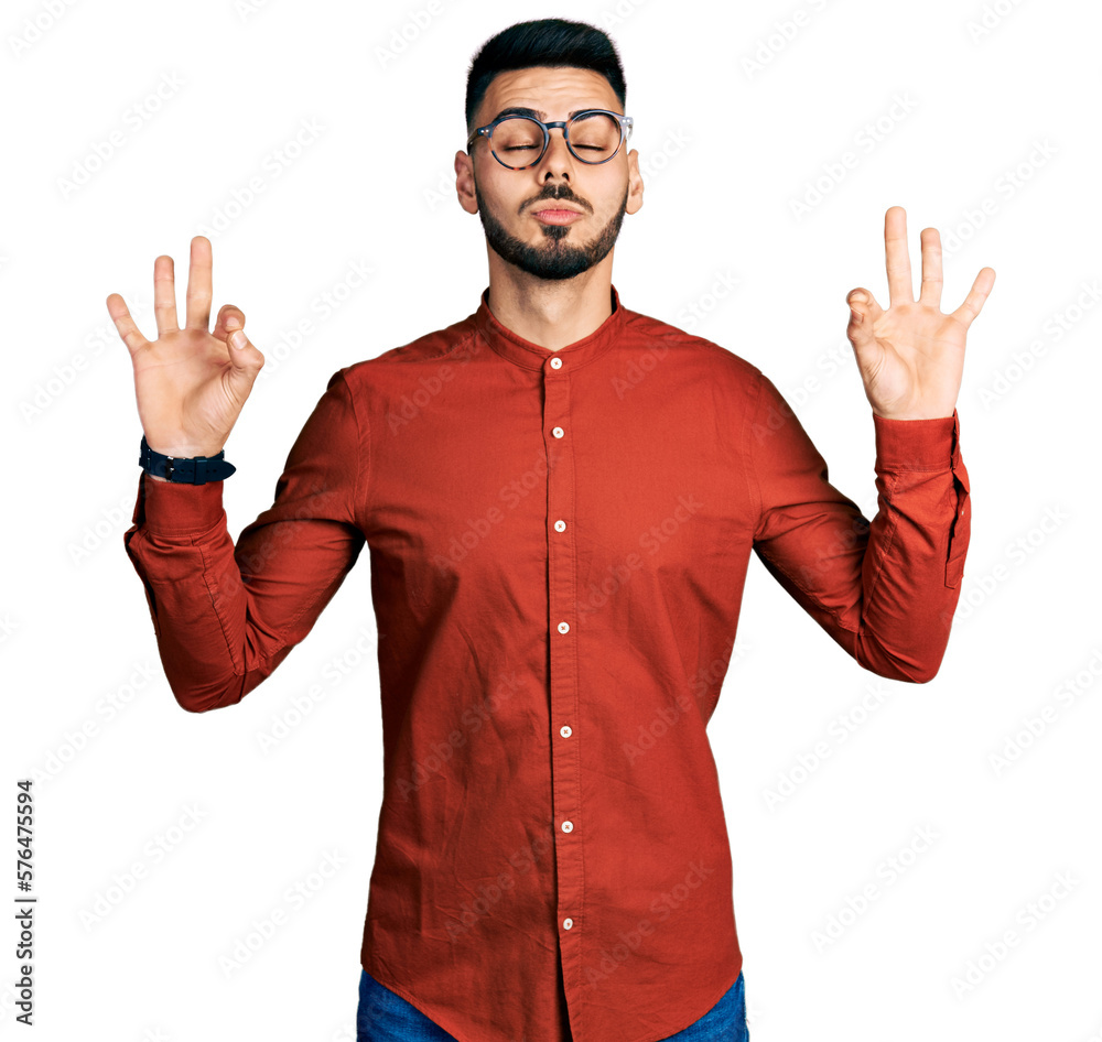 Young hispanic man with beard wearing business shirt and glasses relax and smiling with eyes closed doing meditation gesture with fingers. yoga concept. Young hispanic man with beard wearing business shirt and glasses relax and smiling with eyes closed doing meditation gesture with fingers. yoga concept.