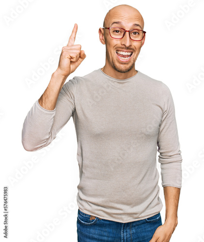 Bald man with beard wearing casual clothes and glasses pointing finger up with successful idea. exited and happy. number one.